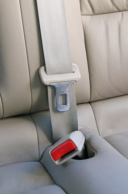 A three-point seatbelt fitted to a pale leather rear seat, showing the shoulder webbing, latch plate and buckle receiver in one view.