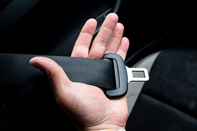 An open hand holding a length of black seatbelt webbing with the metal latch plate resting across the palm.